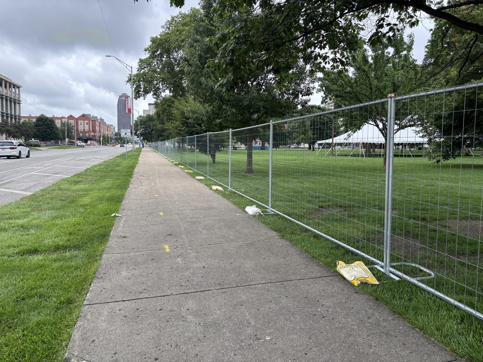 Temporary fence panels on stands along a sidewalk beside a grass lawn