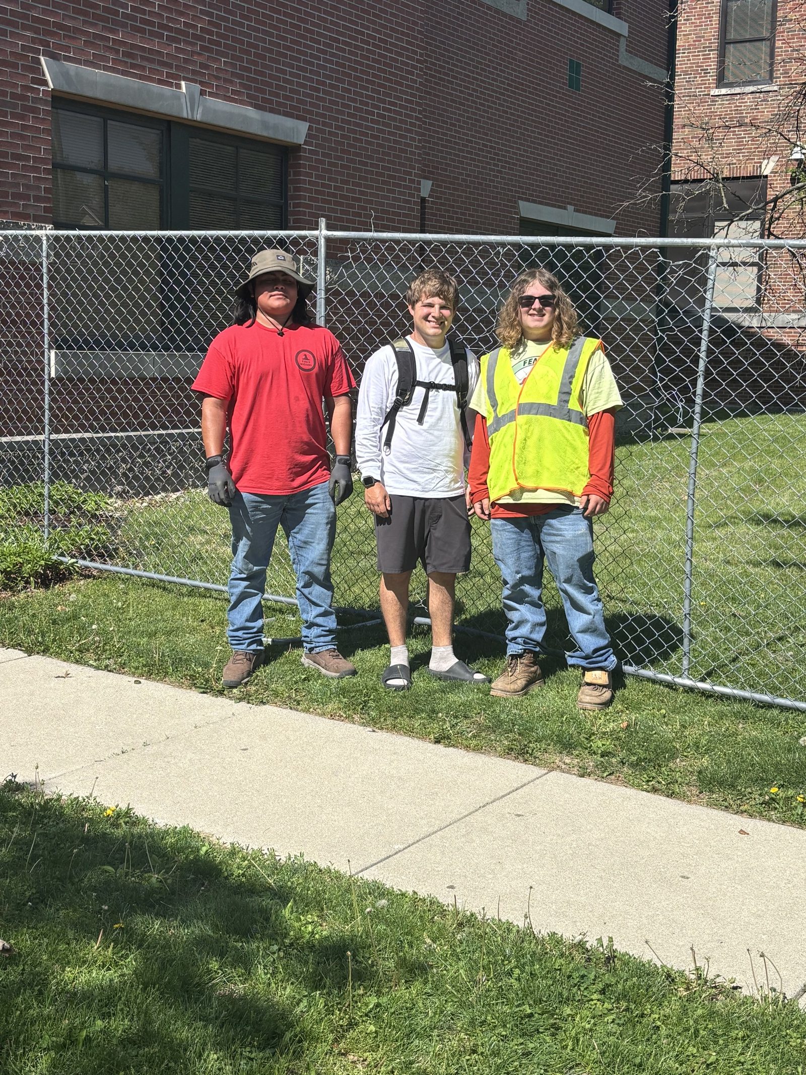 Three members of the Fence Wizards crew standing in front of a chain link fence