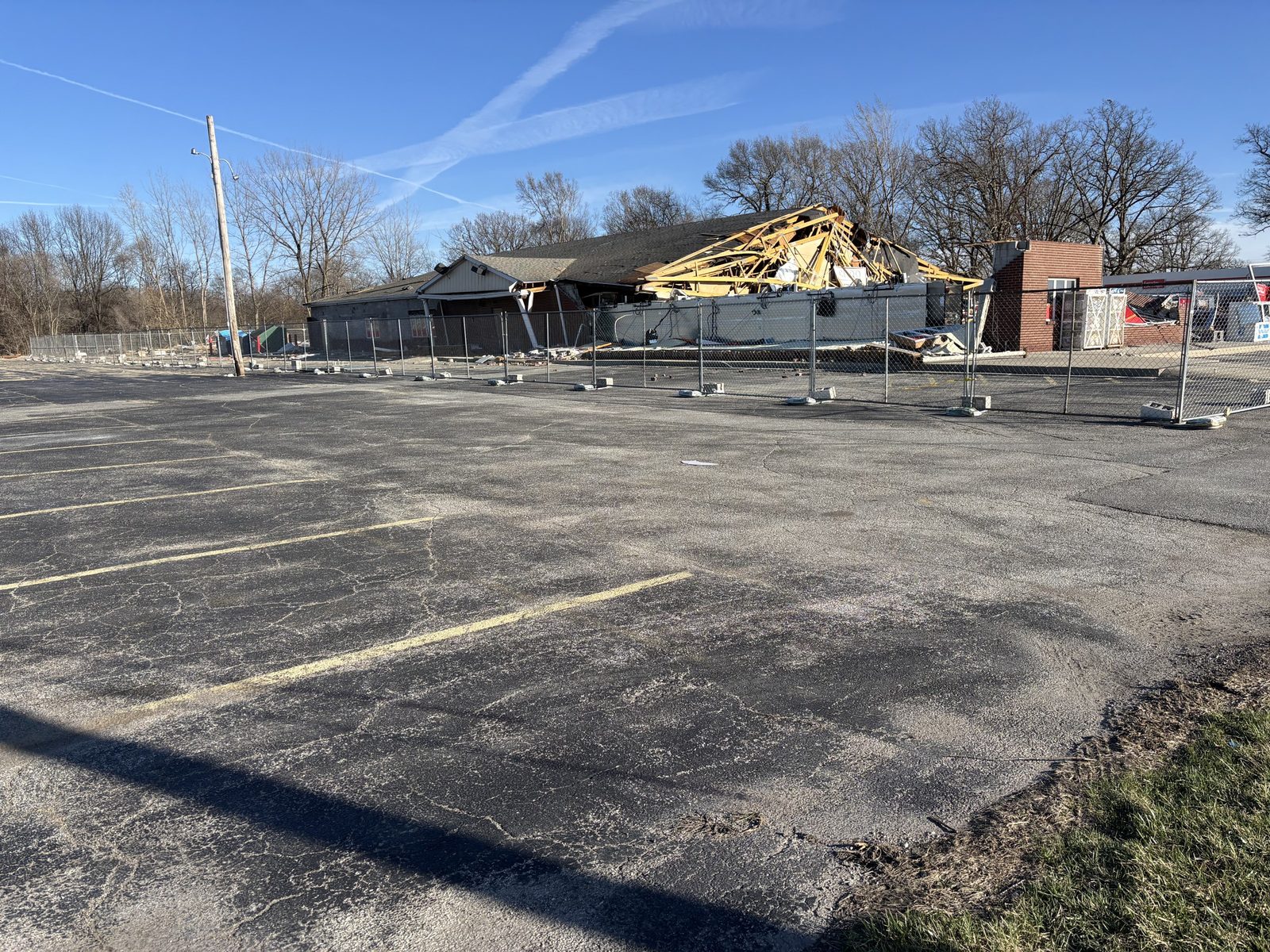 Panel fence around a building with a collapsed roof, seen across an empty parking lot