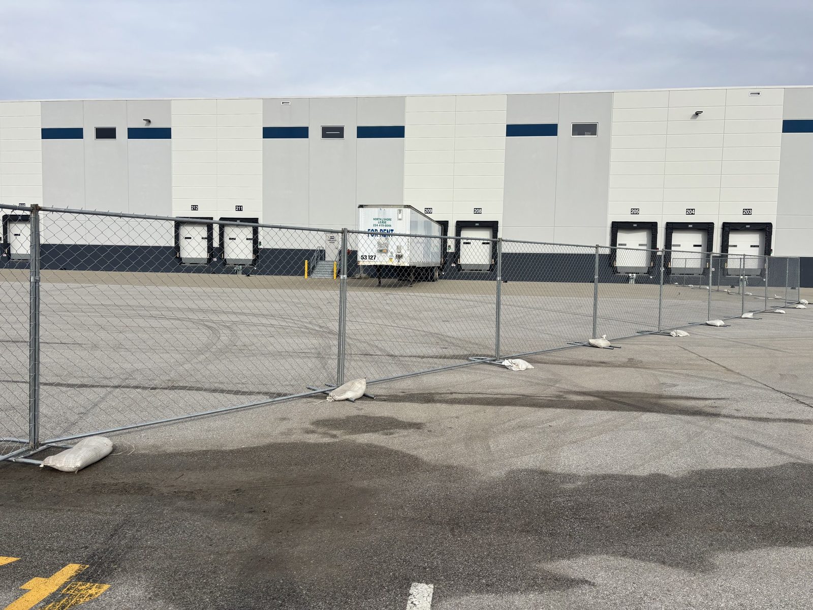 Panel fence across a paved lot in front of a warehouse lined with loading docks