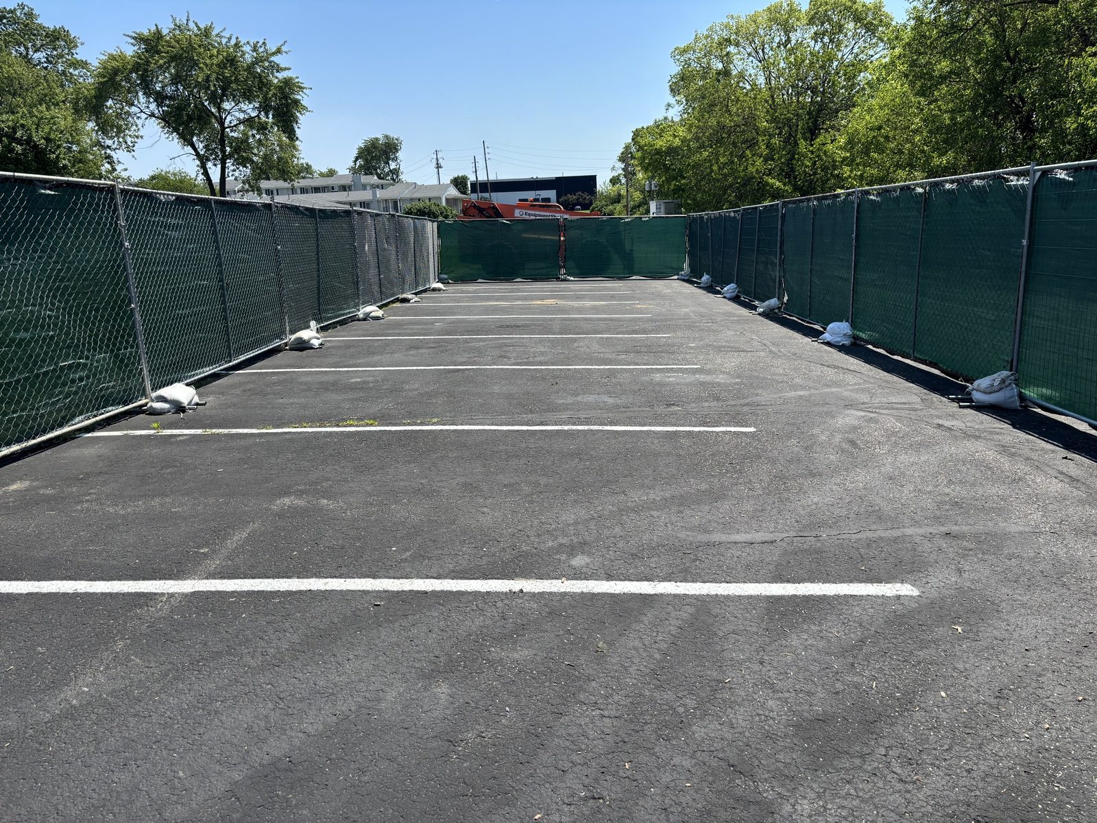 Green windscreen on fence runs along both sides of a parking lot