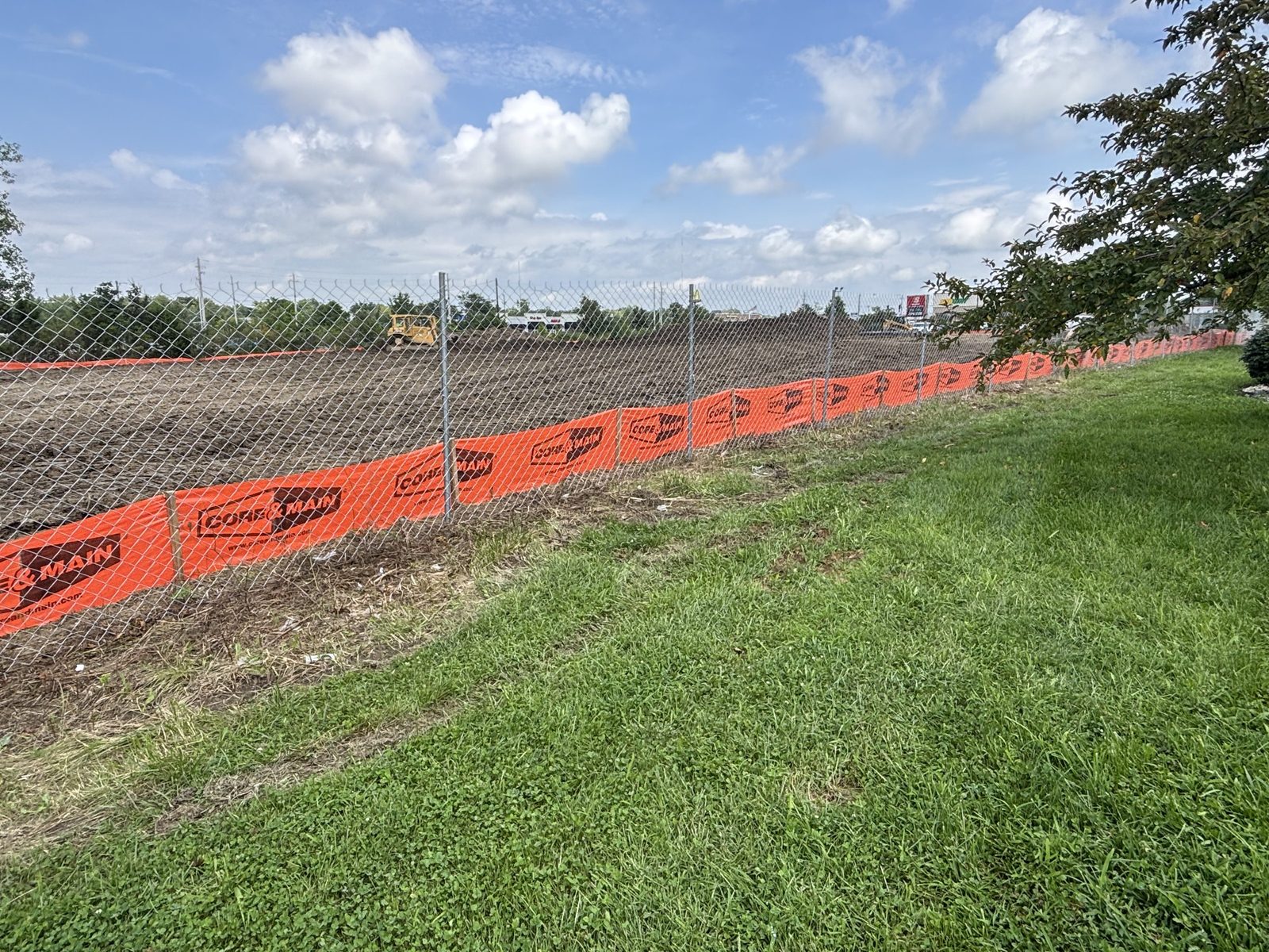 Chain link fence with orange mesh along a graded field