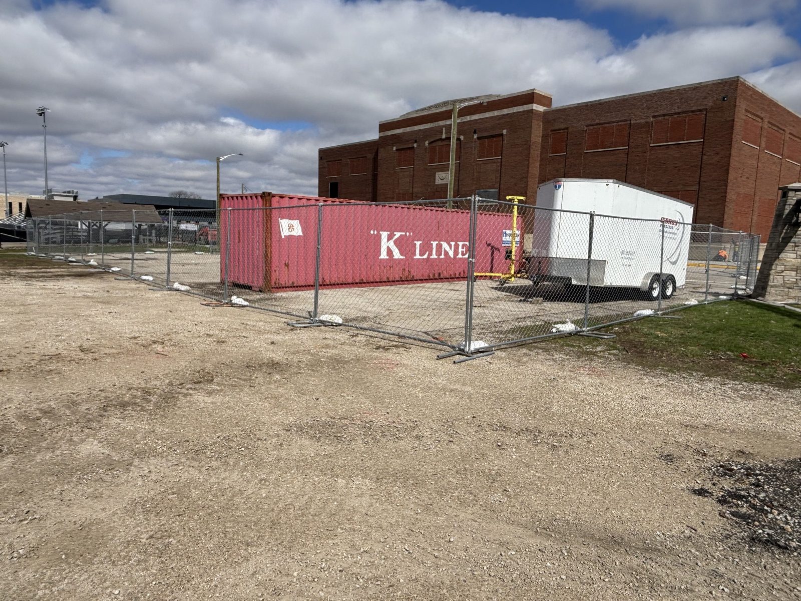 Panel fence around a shipping container and a trailer on a gravel lot