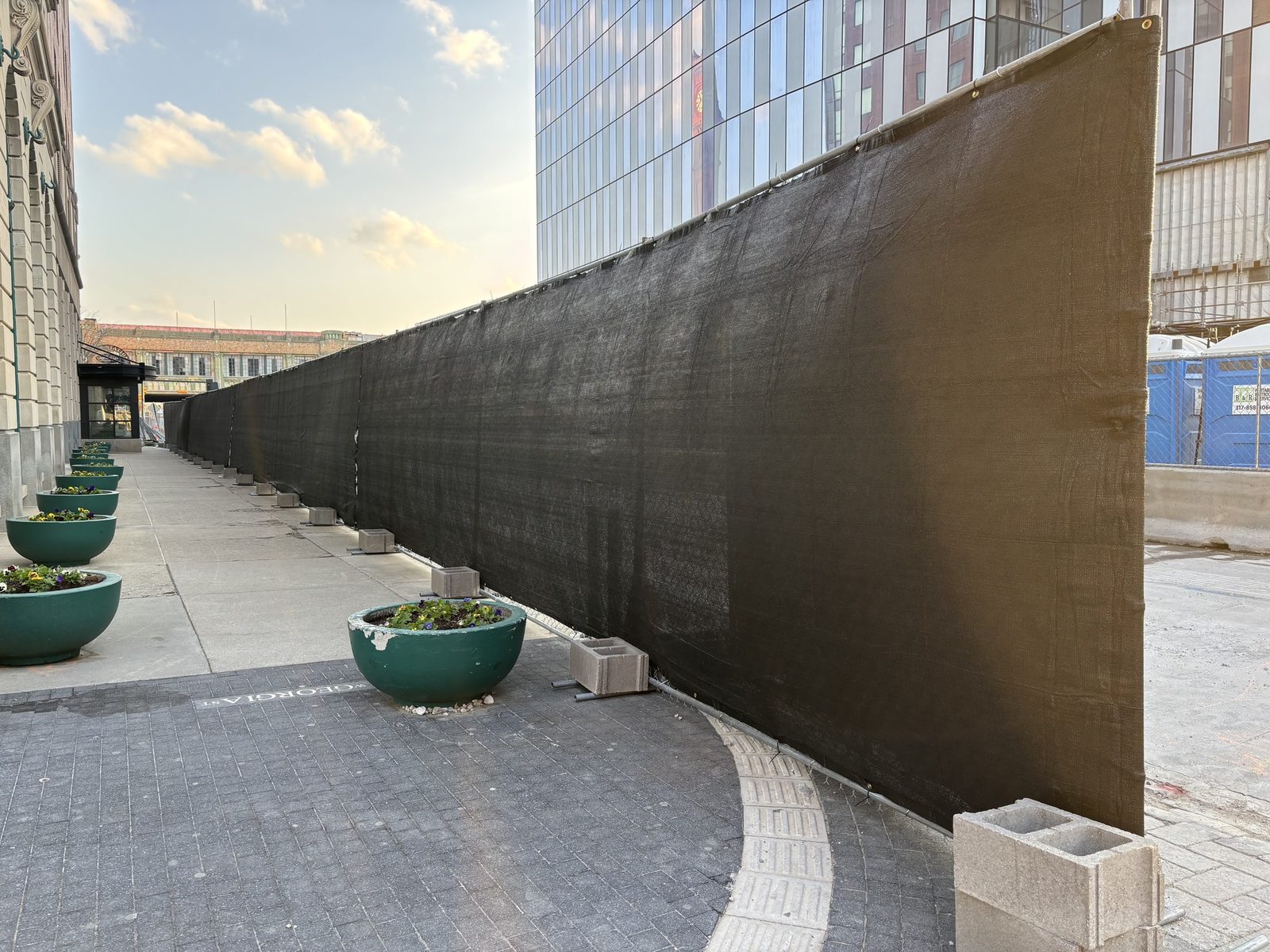 Black windscreen on a fence run curving along a downtown plaza