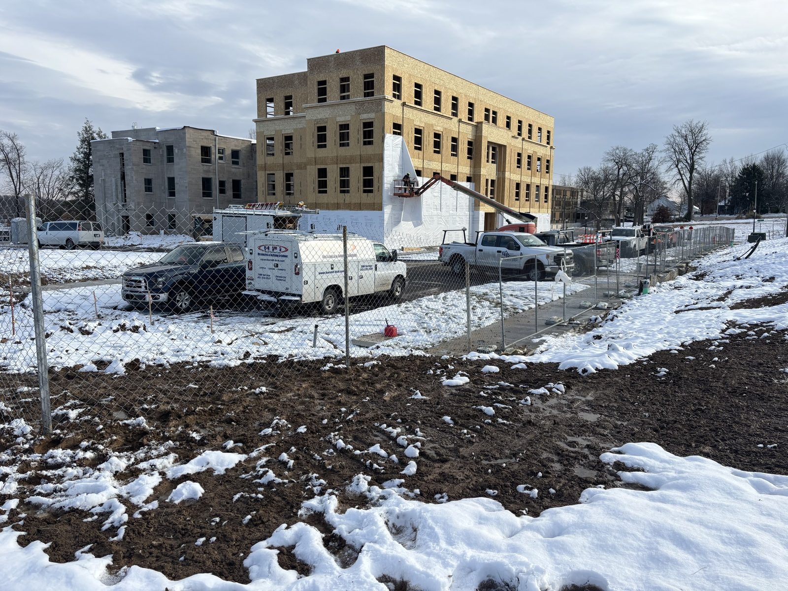 Temporary fence around a snowy building site with work trucks parked inside