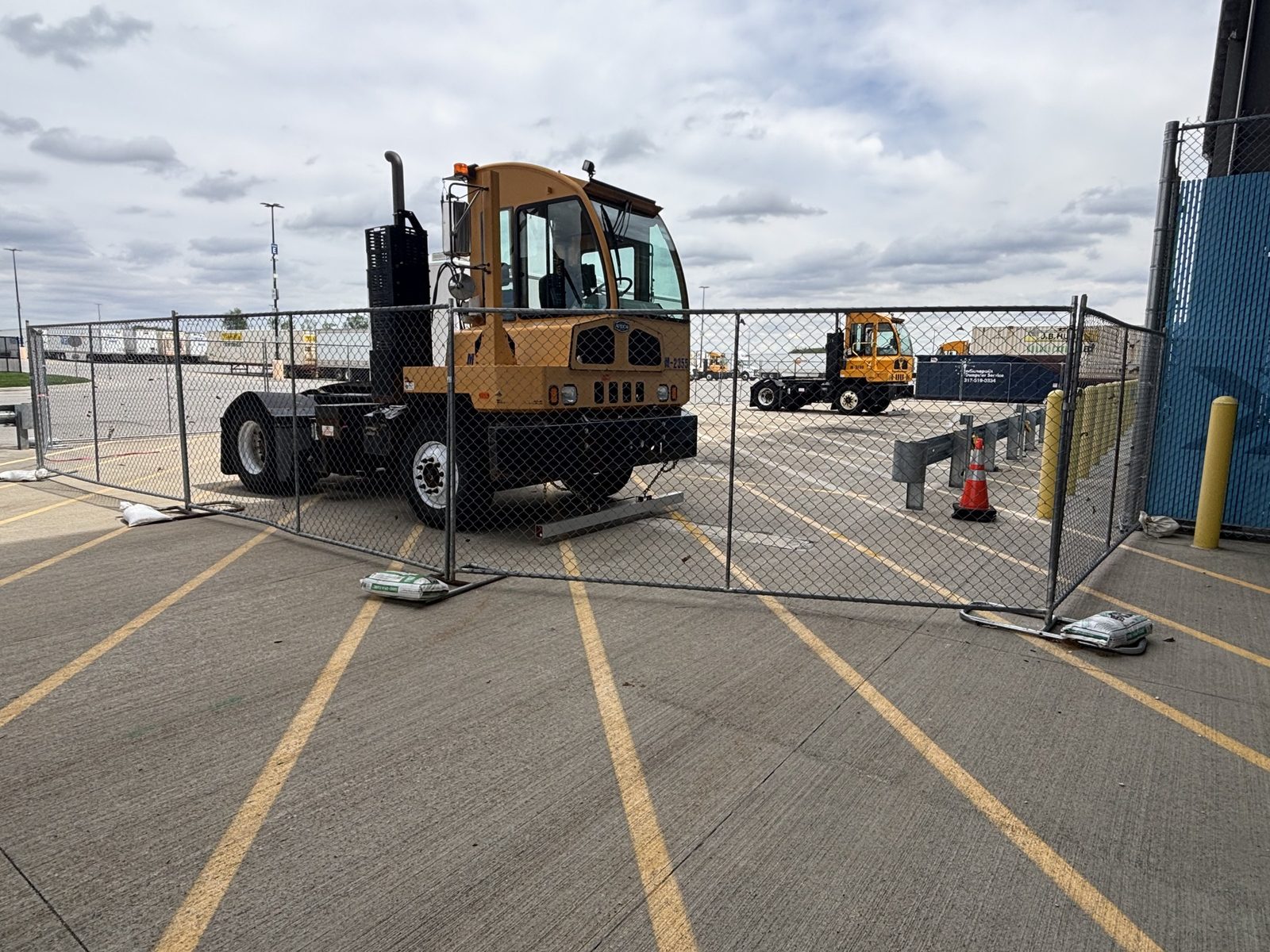Panel fence across a paved truck yard with a yard tractor parked behind it
